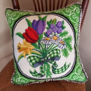 window pane needlepoint pillow with green and white border and a bouquet of daffodil, red and purple tulips, three daisies, and a purple flower with greens and a green and white gingham bow