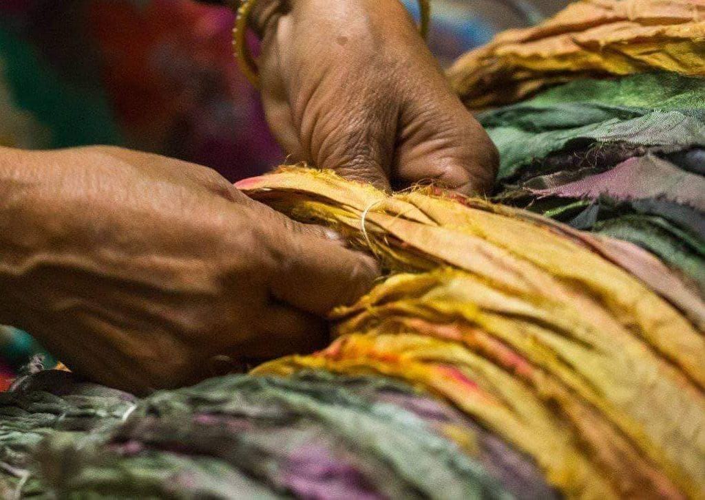 woman weaving strips of repurposed saris to make necklaces